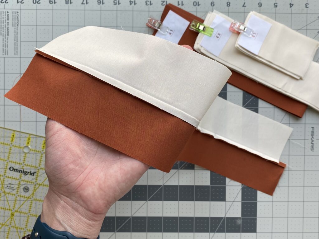 Close-up of two fabric pieces sewn together, with the seam pressed neatly to one side, shown on a cutting mat with additional clipped fabric strips in the background.