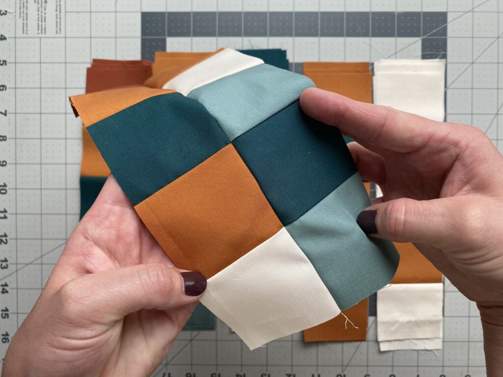 Finished checkered quilt block held in hands, with nested seams creating crisp intersections at the center.